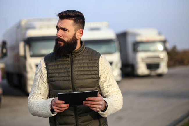 A small business owner stands outside with his fleet in the background reviewing analytics from his fleet fuel card on his computer.