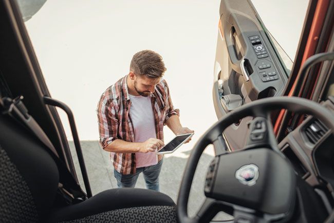 A small business owner stands outside one of his fleet trucks with a tablet reviewing the data from his driver’s fleet card usage.